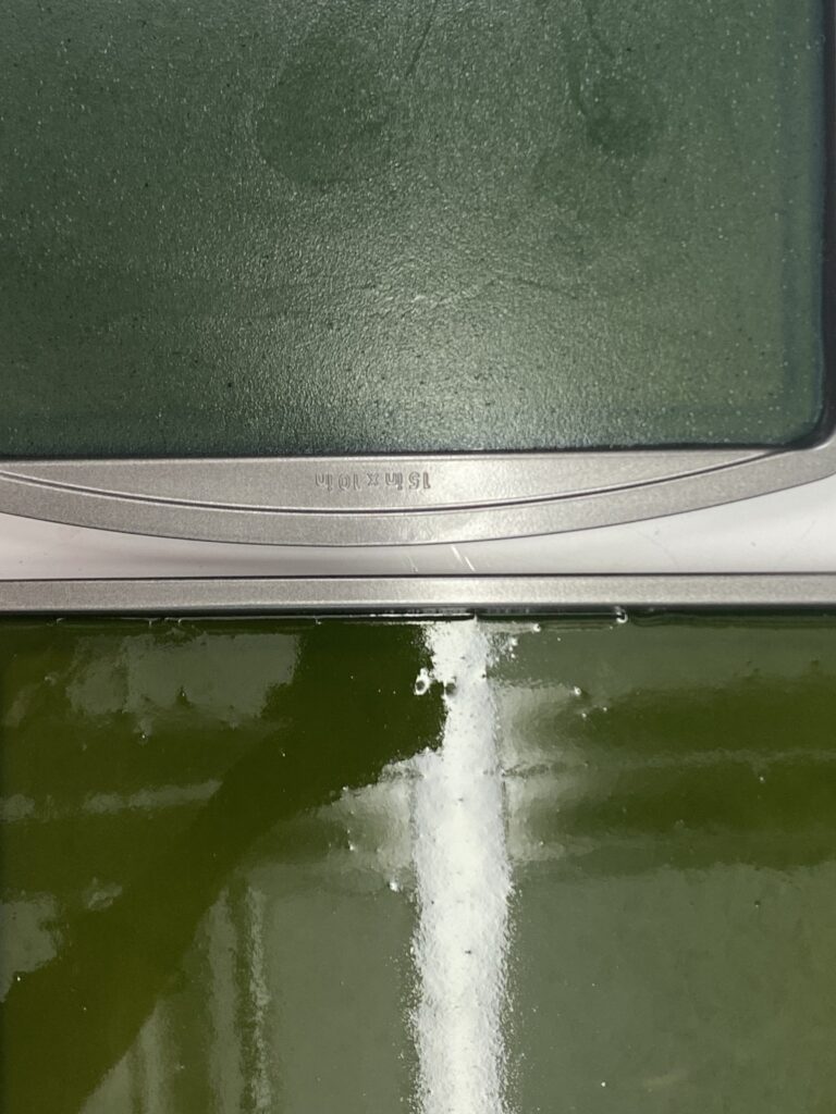 Two baking trays with different shades of green-dyed bioplastic.