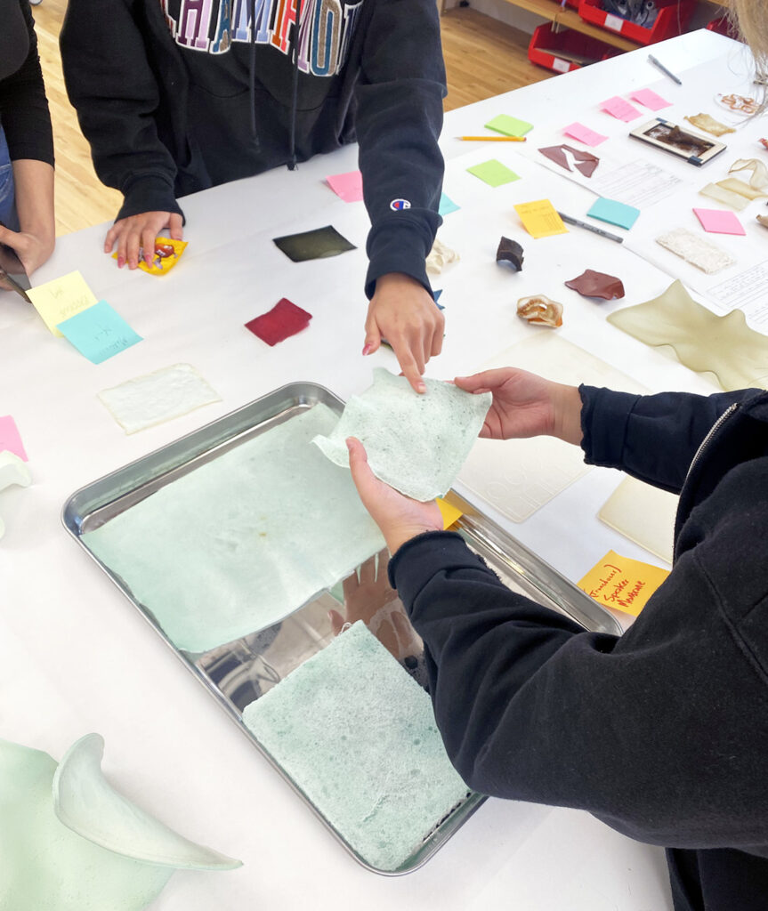 Snapshot from Material Kitchen's bioplastic ideation session. Many colorful material swatches are on a table, hands are touching the materials.