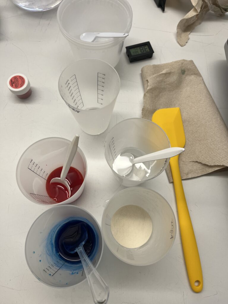 Plastic measuring cups with colored water and agar agar powder.