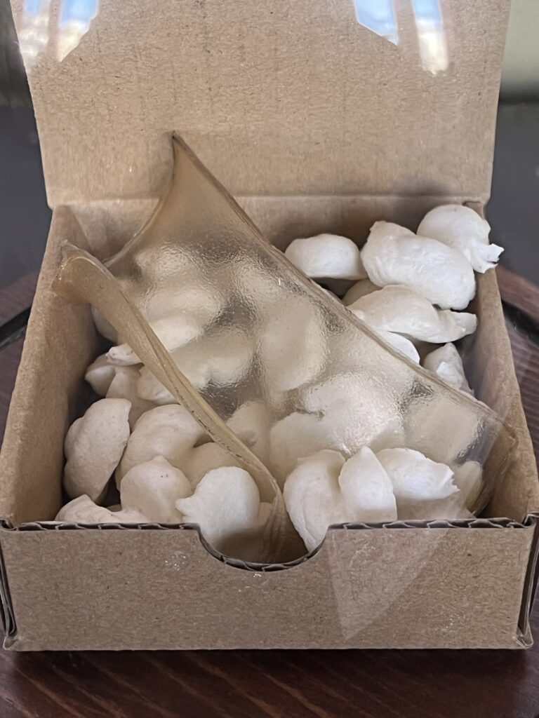 Biofoam packing "ducks" supporting a fragile piece of bioplastic in cardboard box.