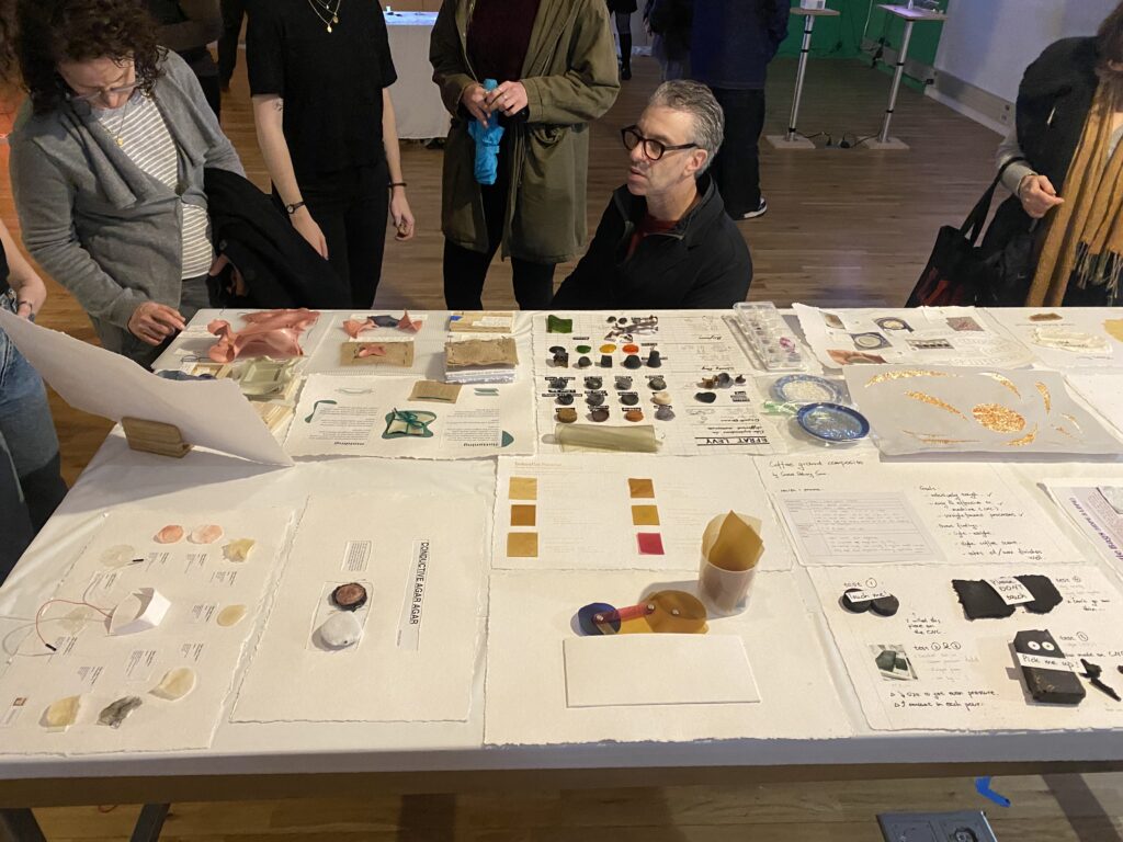 Viewers engaging with table full of students biomaterial swatches and documentation at the ITP Winter show.