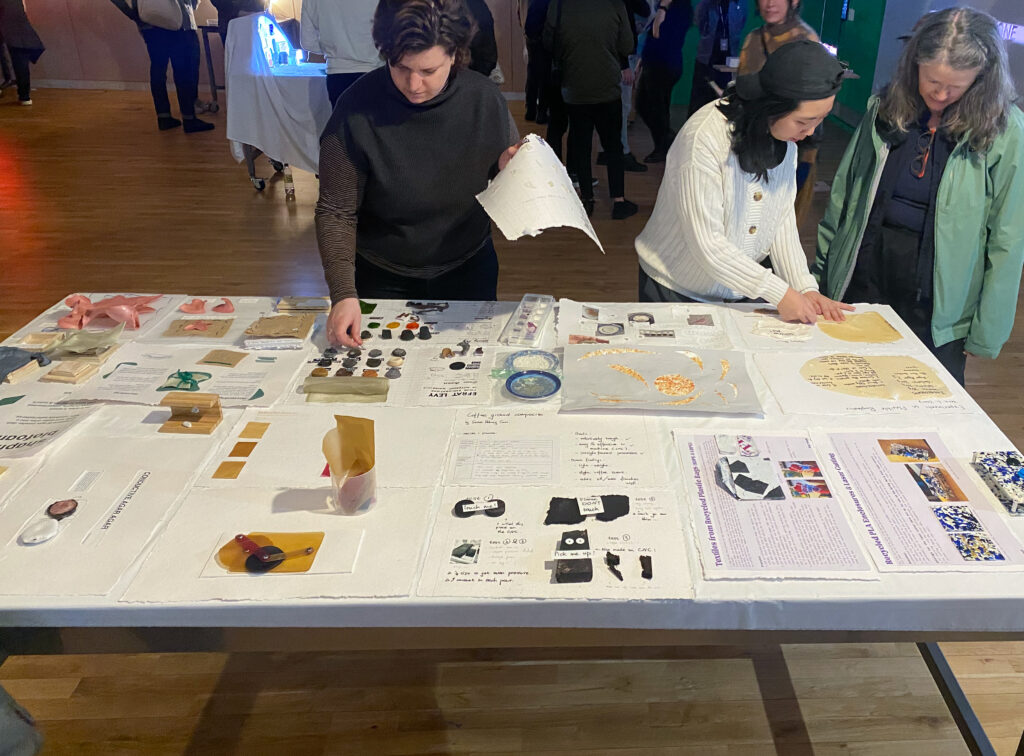 Viewers engaging with table full of students biomaterial swatches and documentation at the ITP Winter show.