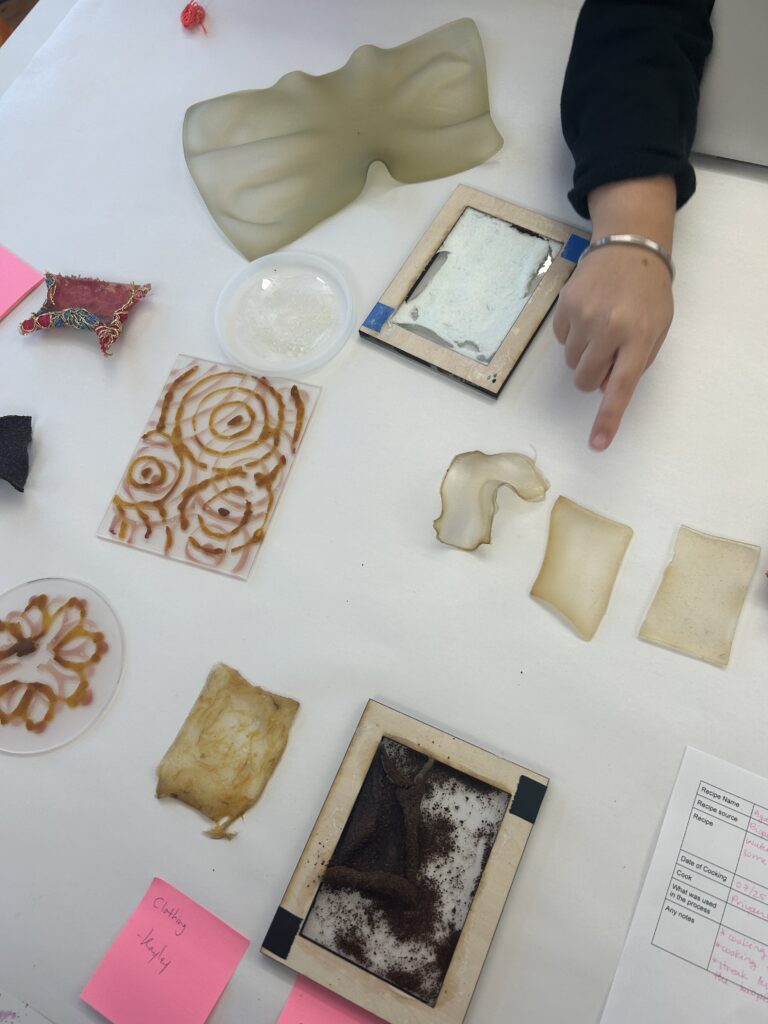 Table full of various bioplastic swatches, a hand points one out.