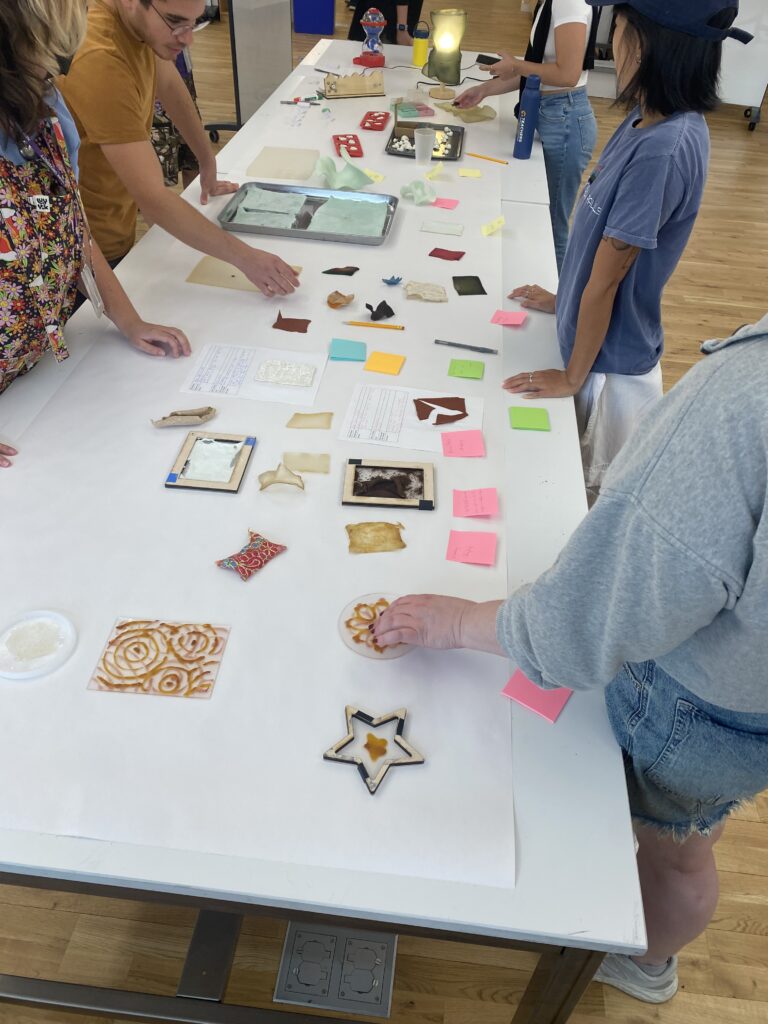 Students investigating a table full of colorful bioplastic swatches and sticky notes.