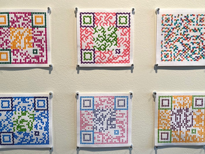 six QR codes drawn by hand, hanging on an off-white wall