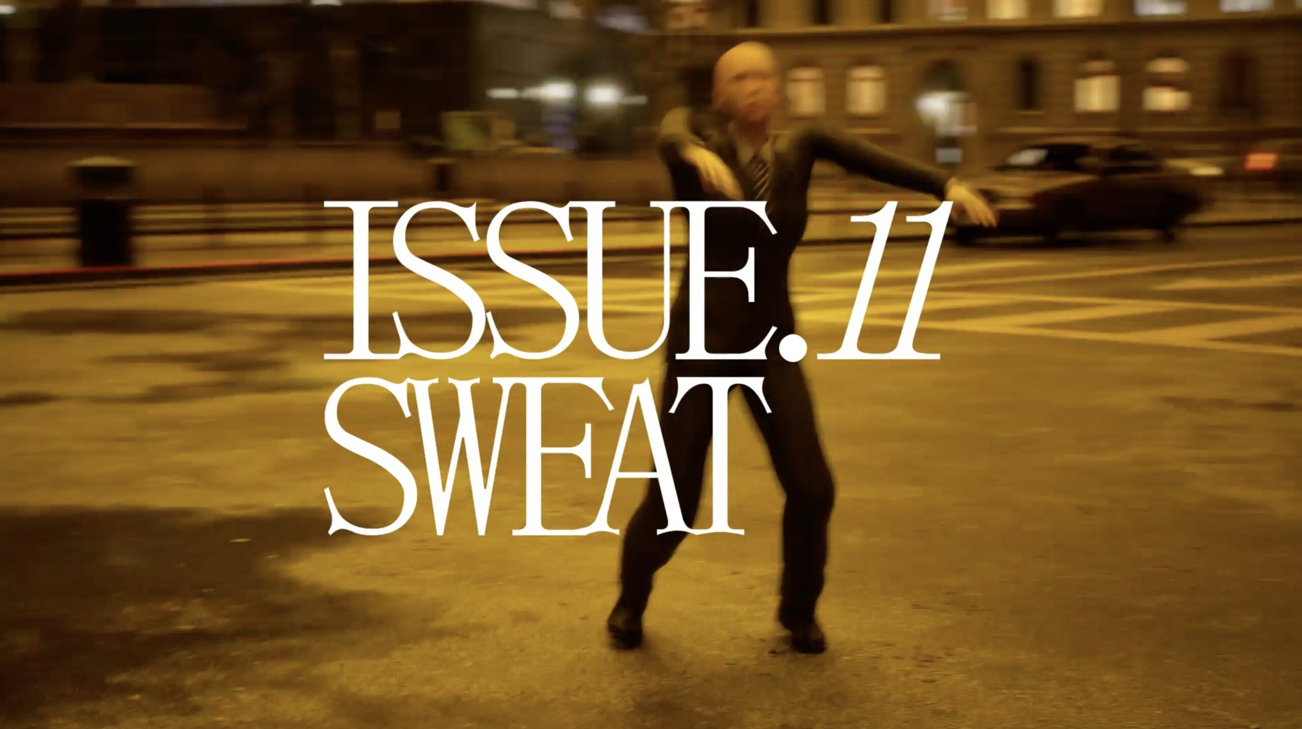 a person dressed in a black suit dancing in the middle of the street behind a white lettering says "issue 11 sweat"