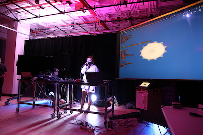 An ITP camper presenting code and graphics on a screen in a room with purple lighting.
