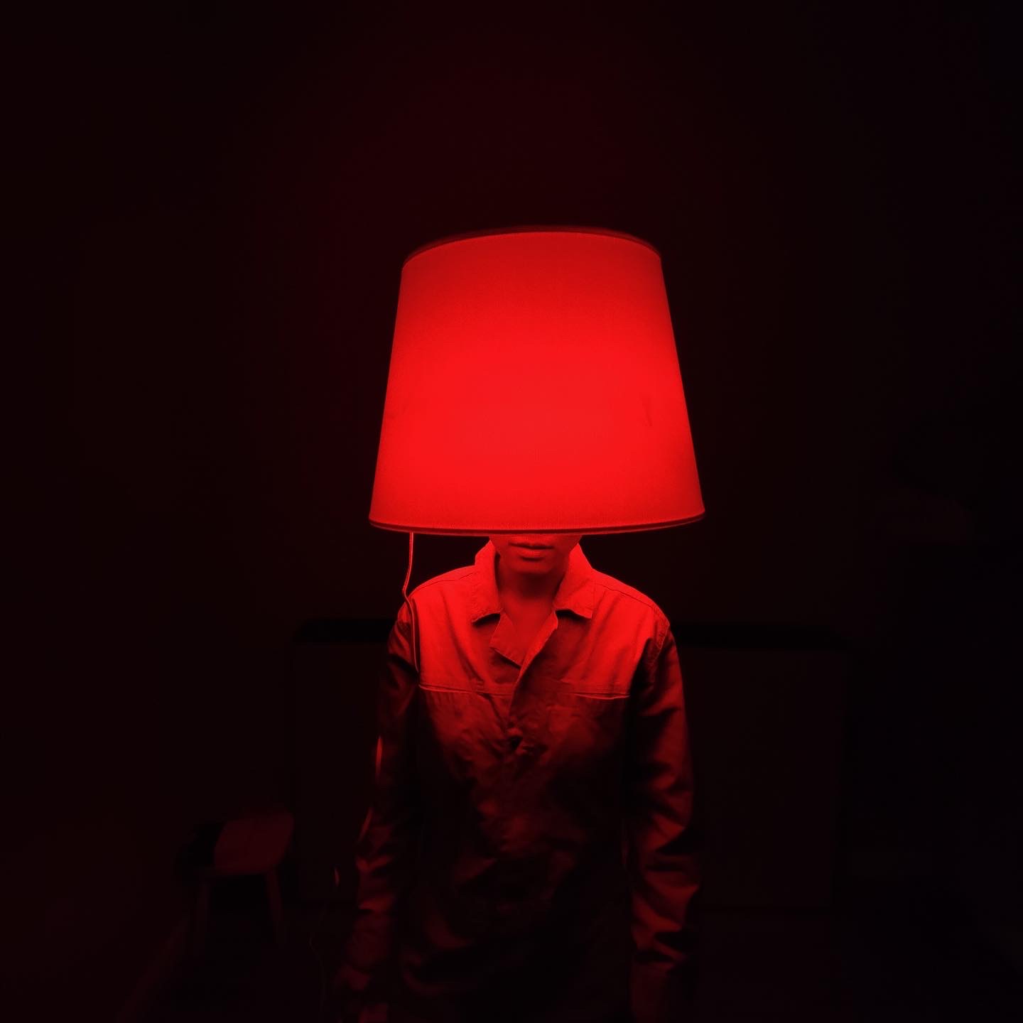 Person illuminated in red with a lamp shade on their head