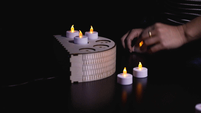 A video of "Grim Grinning Ghosts", by Leia Chang. Someone places glowing candles into a candleholder. Ghosts then appear on a screen, and the candles pop out.