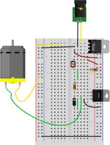 Breadboard drawing of a transistor controlling a DC motor with a pushbutton. The drawing is similar to the breadboard drawing with the potentiometer, but the potentiometer has been removed and a light-dependent resistor is now in rows 6 and 9 in the right center section, A fixed 10-kilohm resistor connects row 9 to the ground bus on the right side. A green wire connects row 9, to row 12 where it connects to the transistor's 1-kilohm resistor. 