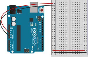 An Arduino Uno on the left connected to a solderless breadboard, right. The Uno's 5V output hole is connected to the red column of holes on the far left side of the breadboard. The Uno's ground hole is connected to the blue column on the left of the board. The red and blue columns on the left of the breadboard are connected to the red and blue columns on the right side of the breadboard with red and black wires, respectively. These columns on the side of a breadboard are commonly called the buses. The red line is the voltage bus, and the black or blue line is the ground bus.