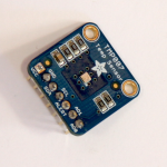 A TMP007 Temperature sensor module. There are 6 pins along the bottom, labeled GND, SDA, SCL, Alert, AD1, and AD0 (left to right)