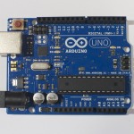 An Arduino Uno. The USB connector is facing to the left, so that the digital pins are on the top of the image, and the analog pins are on the bottom.