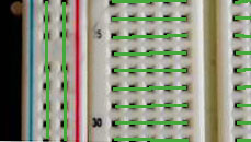 A close-up picture of the front of the breadboard. The green lines indicate which holes are connected by a metal strip behind. Each short horizontal group of five holes is connected, and each long vertical group of holes is connected. The vertical groups are not connected to each other or to the horizontal groups, however. 