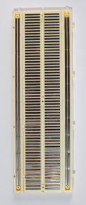 The back of a breadboard with the adhesive backing removed, showing the metal strips underneath. Each long row down the side has a continuous metal strip underneath, running vertically down the board. The metal strip connects all the holes in its row. The holes of the short rows are connected with short metal strips running perpendicular to the long strips on the side. There is a break in the middle of the board, so that there is no connection between the right side and the left side. 