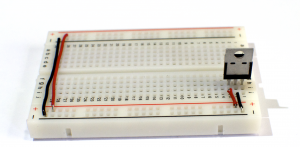 Close-up showing a 7805 5-volt voltage regulator connected to a breadboard. The breadboard is oriented so that the long rows are horizontal this time, and you are looking at the back of the regulator. The regulator is connected to the right-most three rows of the board. 
