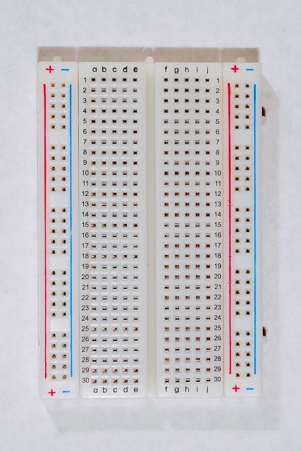 A photo of a short solderless breadboard with two rows of holes along each side. There are no components mounted on the board. The board is oriented sideways so that the long rows of holes are on the top and bottom of the image.