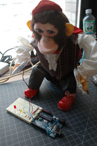 A mechanical toy monkey that plays cymbals. The cymbals are covered with aluminum foil. The foil is connected to wires, and the wires are connected to an Arduino and breaboard. The two wires from the cymbals act as a switch when they are hit together.