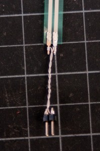 Photo of the metal ends of a force-sensing resistor with wire-wrapped wiring. Very thin single-strand wire is wrapped tightly around each of the two metal connections of the sensor, making a tight connection with no soldering.