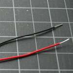 Photo of two pieces of 22AWG hookup wire. The wire is approximately 0.05 inches (1mm) in diameter, and clad in a plastic insulation. These two wires have red and black insulation, respectively.