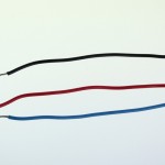Three short pieces of hookup wire: one is clad in red insulation, one in blue, and one in black. All three have exposed ends approximately 5mm long.