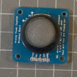 Photo of a breadboard-mountable joystick, This component is mounted on a printed circuit board that's about 4cm on each side. The joystick itself is about 6cm tall, controllable by a thumb. There are five pins on one side of the PCB for mounting on the breadboard.