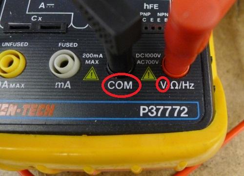 Photo of the bottom half of a multimeter, showing the holes for the test leads. The left hole, labeled A, is empty. The center hole, labeled COM, has the black lead in it. The right hole, labeled VΩmA, has the red lead in it. 