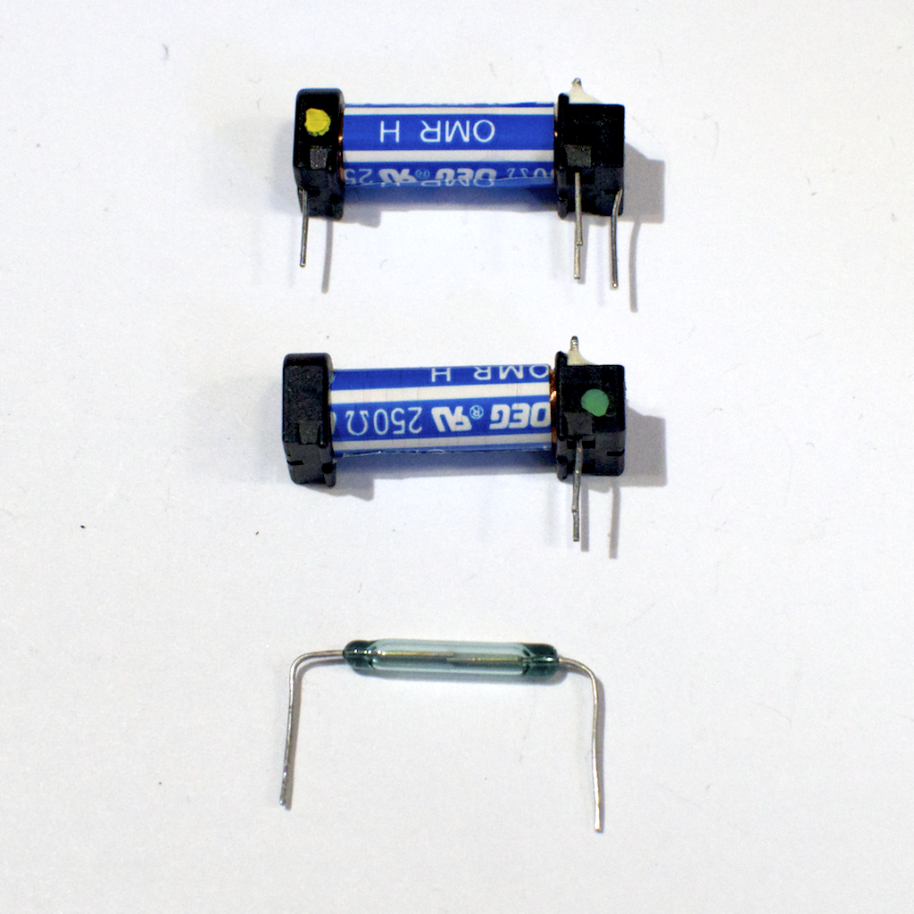 Two relays, one whole and the other with the switch removed. The blue and white tube is the coil, and the green tinted glass vial contains the internal switch
