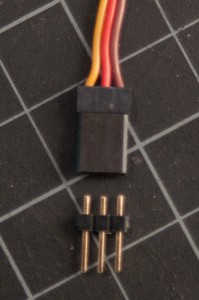 Photo of a servomotor connector with three header pins next to it. The header pins appear too short to connect properly to the servomotor connector.
