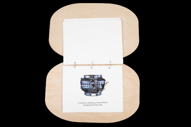 A book flipped open to a page with a teapot shown, including a piece of plastic that feels like a teapot. Text reads,