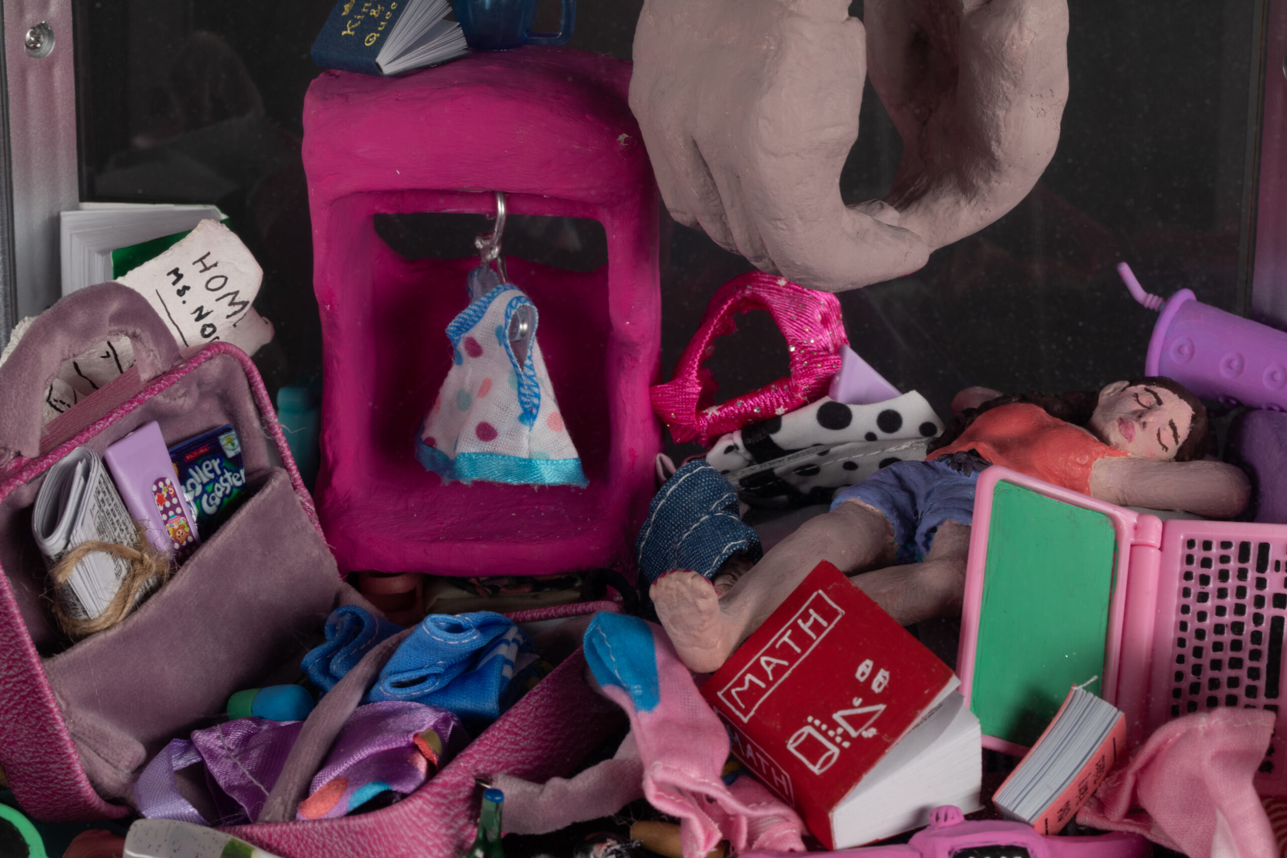 A closeup of the claw machine sculpture. The person is lying in bed inside the machine and it is surrounded by clutter