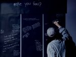 A person answering the question "how did the experience make you feel"? on a black sheet presented before them.