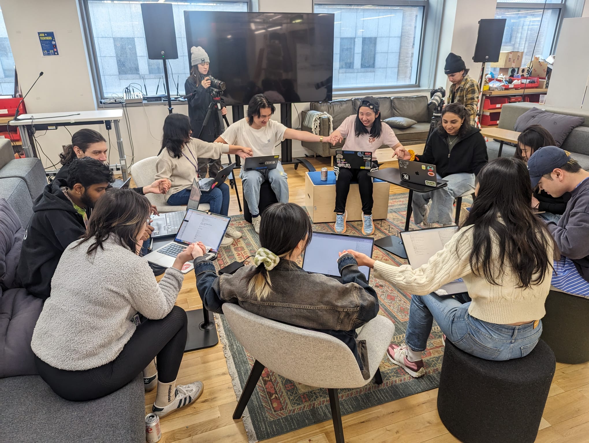 Group of students sitting in a circle holding hands in front of their laptop