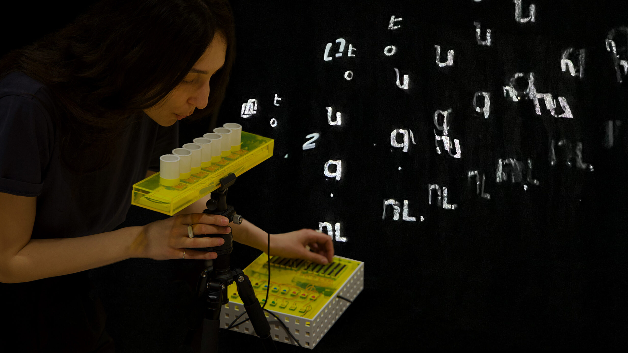 A person blows into the Lezu while playing a MIDI-style controller, surrounded by tulle layers reflecting the Armenian ABC.