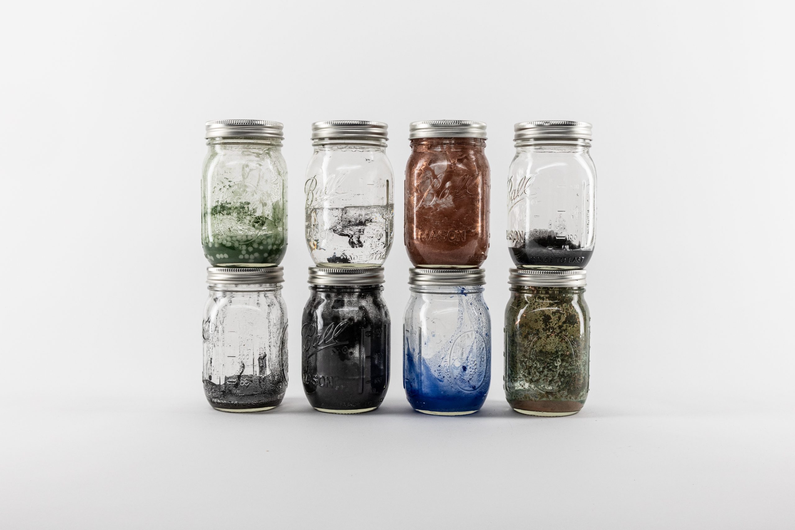 Eight paints stored in jars, stacked on each other in front of a white background