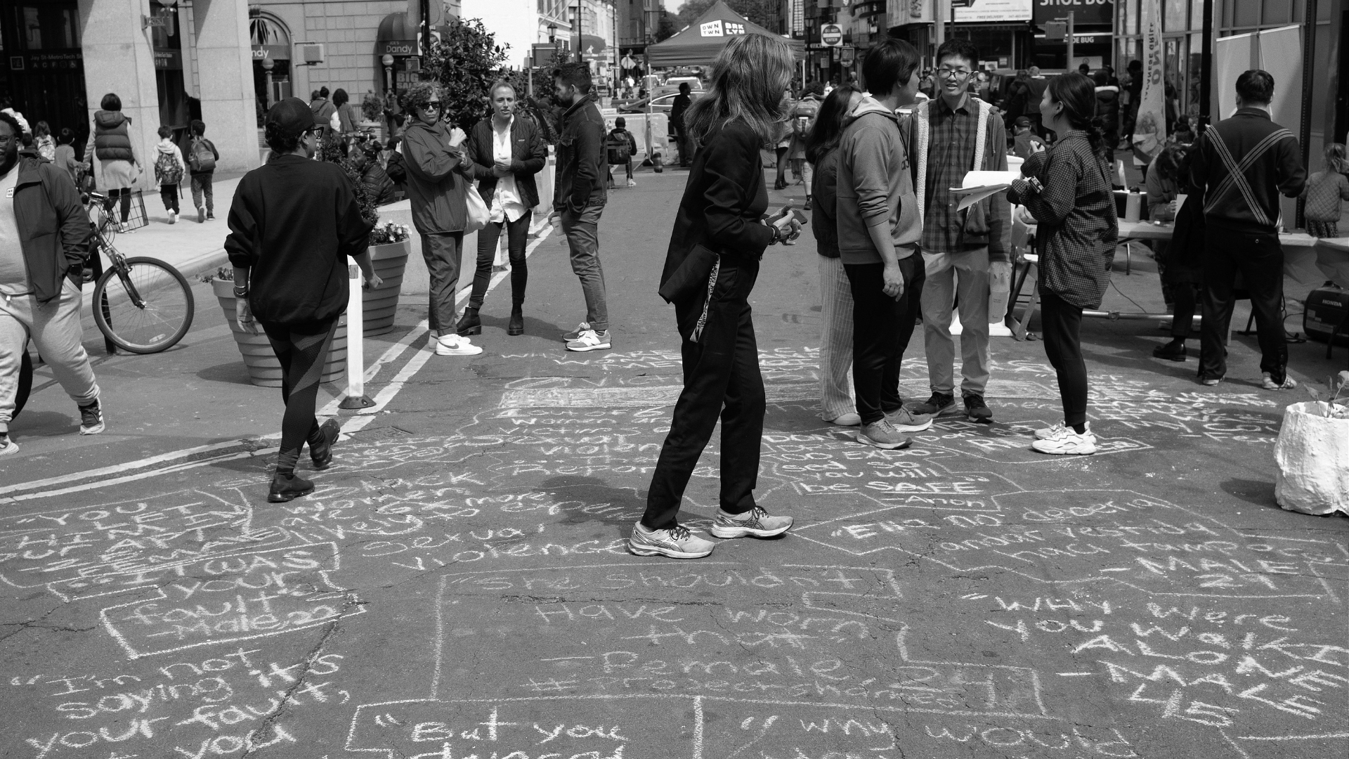 a street full of quotes written in chalk while people walk by it.