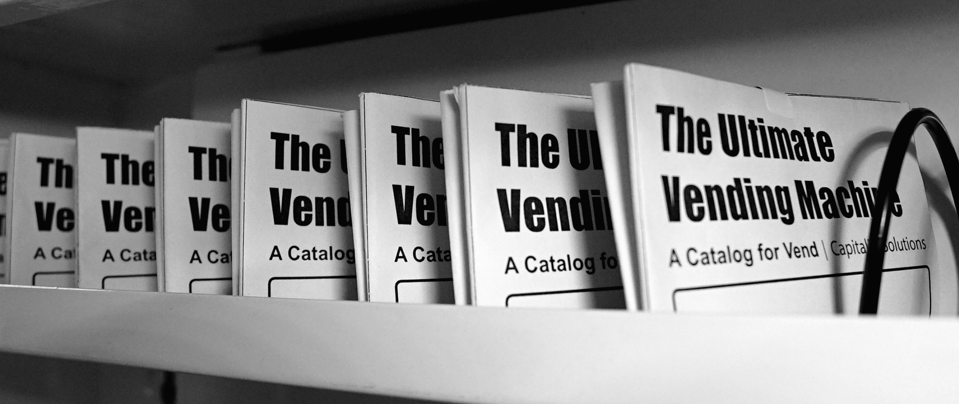 The Catalog Volume One on display in the row of the Ultimate Vending Machine. The Catalog are folded and organized for the display.