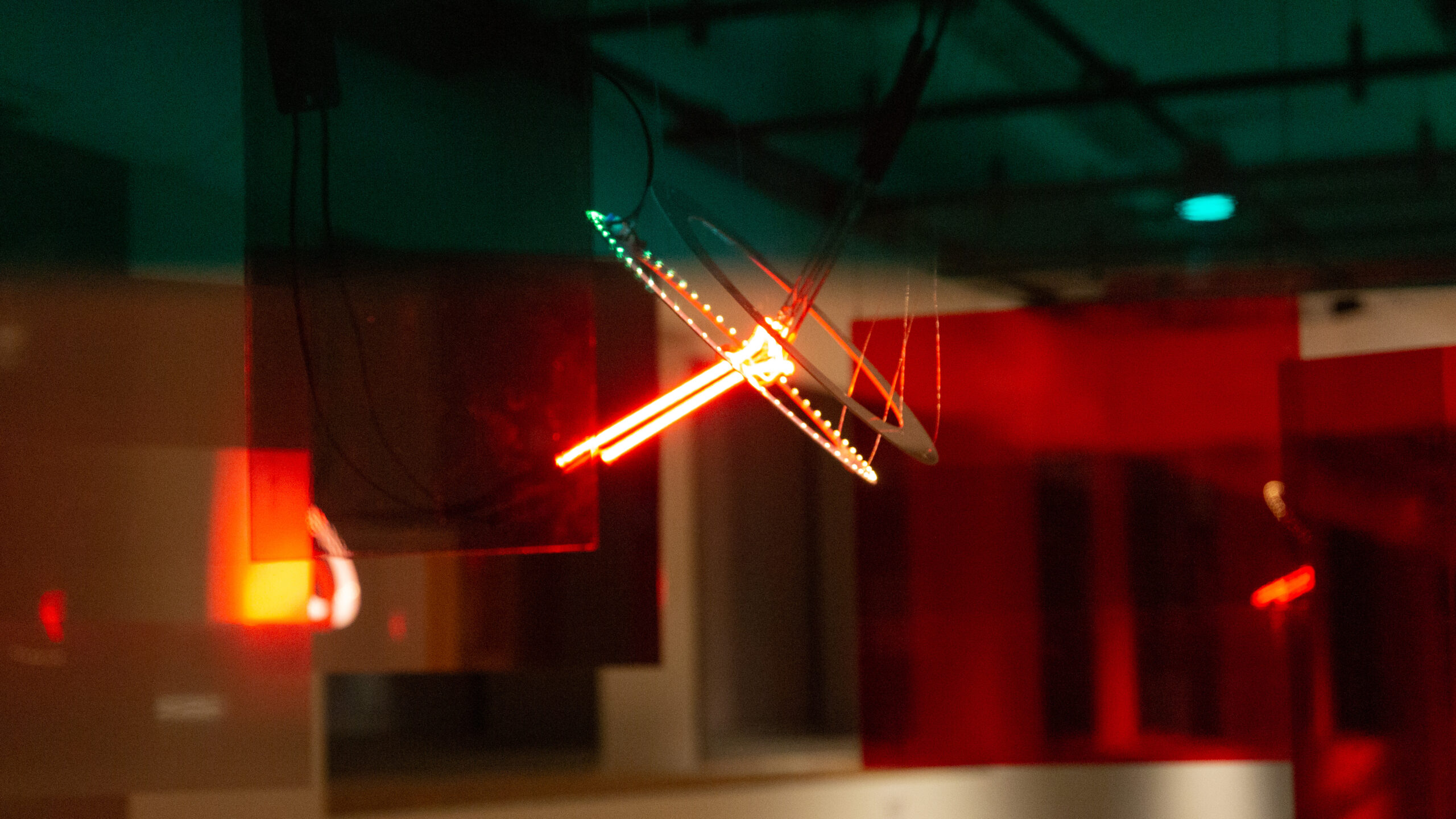 A suspended light sculpture with two neon pieces and two printed circuit boards, featuring gray translucent acrylic panels that reflect the light sculpture in the background.