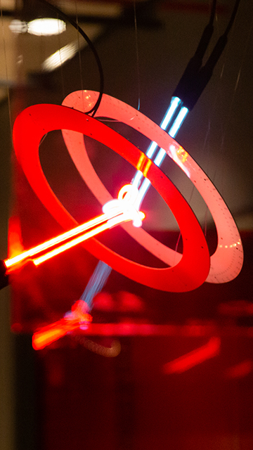 2 pieces of neon, one red and one blue, form a knot in the middle, with 2 white, ring-shaped printed circuit boards that reflect the neon light.