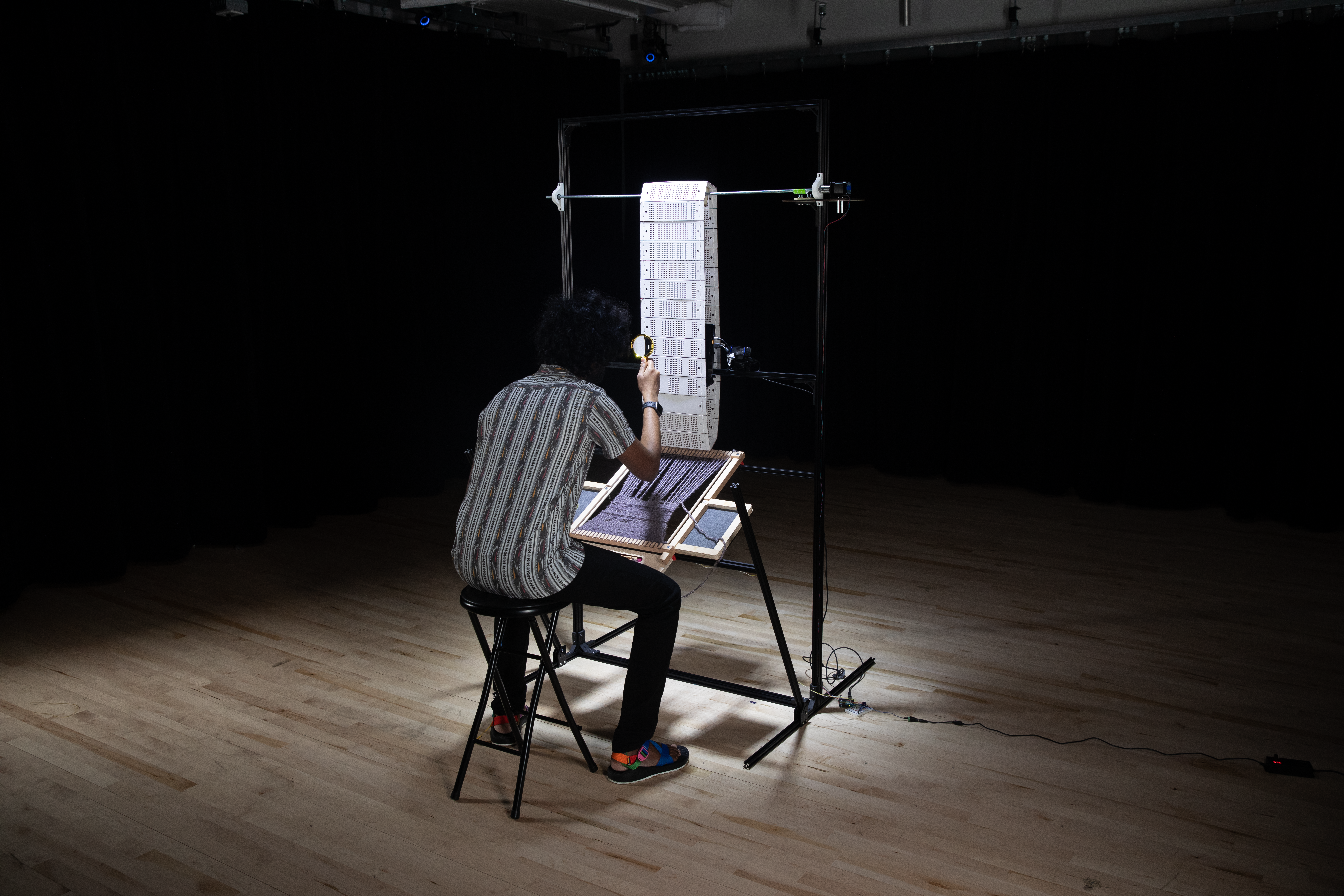 The installation with a participant sitting on the stool in front of it and looking at the faces through the cards using a magnifying glass.