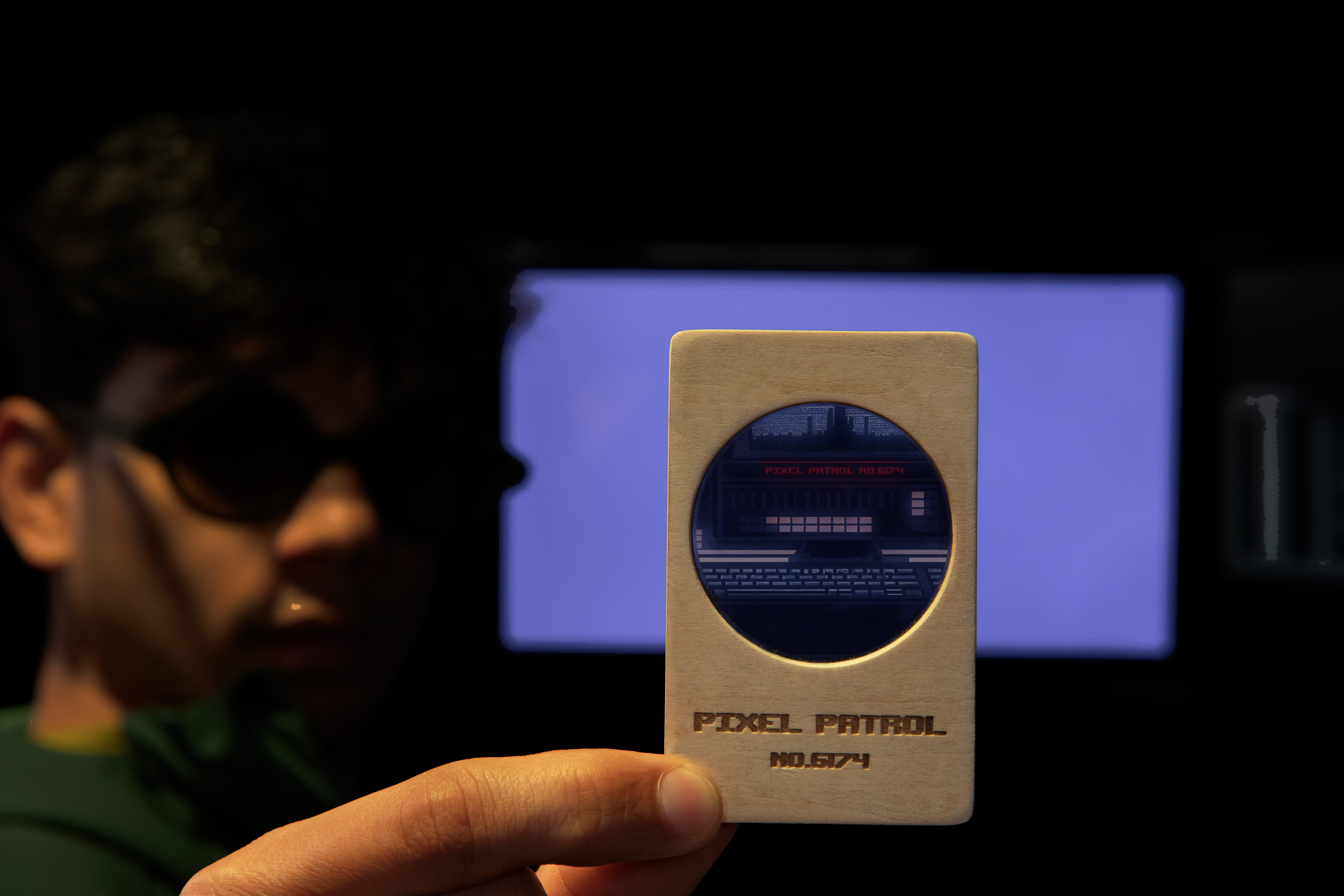 A participant holding a polarizing card up to one of the monitors on the three-monitor setup in Pixel Patrol. The polarizing card is used to reveal hidden content and enable the participant to view the screens.