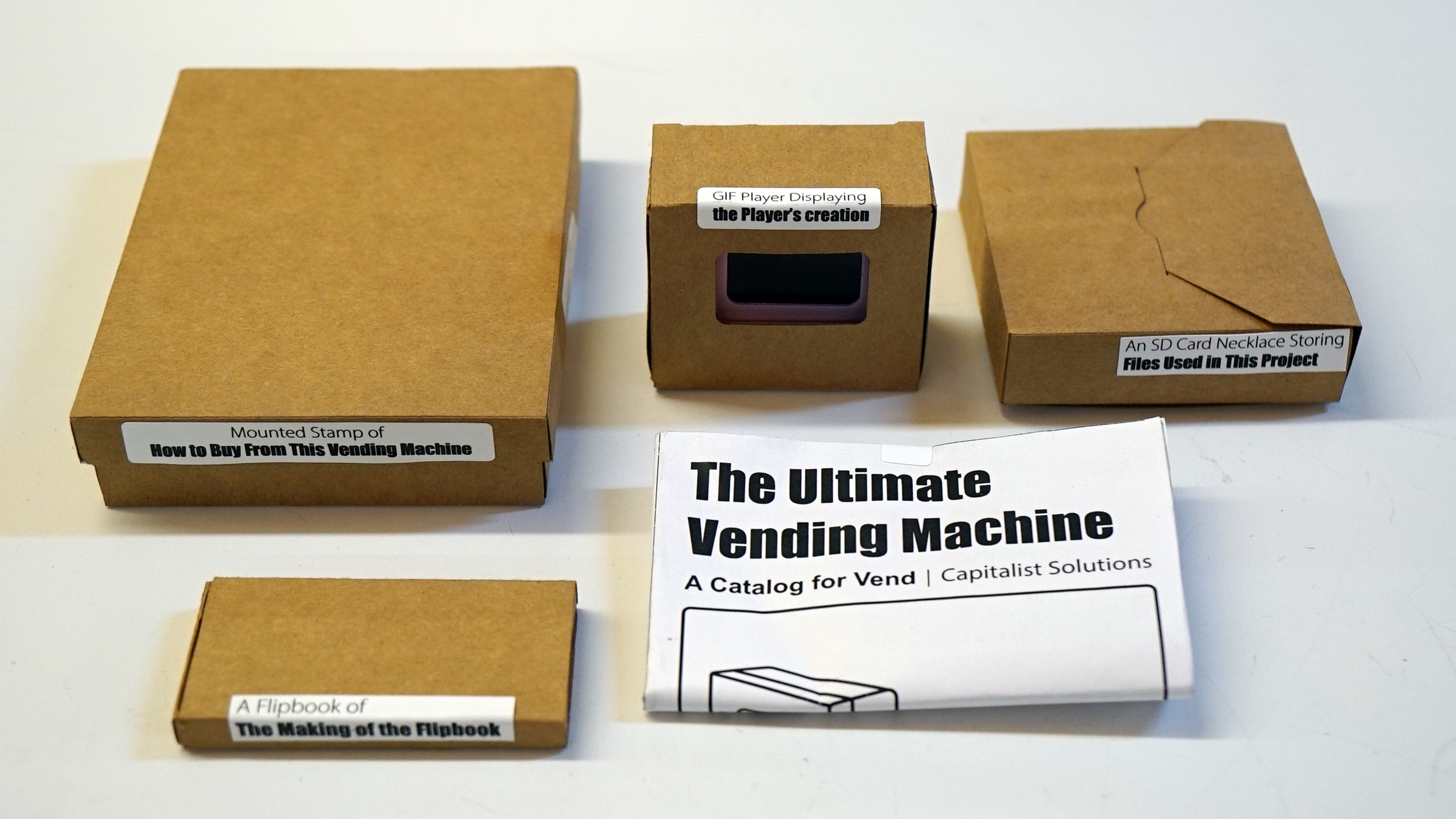 The 5 products of the Ultimate Vending Machine displaying on a table. They are labeled with their name. They are (from left to right, top to bottom): The mounted stamp of how to buy from the vending machine, the Mini GIF player playing the player's creation, The SD Card necklace that contains all the files used, the flipbook of the making of the flipbook, The Ultimate Vending Machine Catalog Volume One.