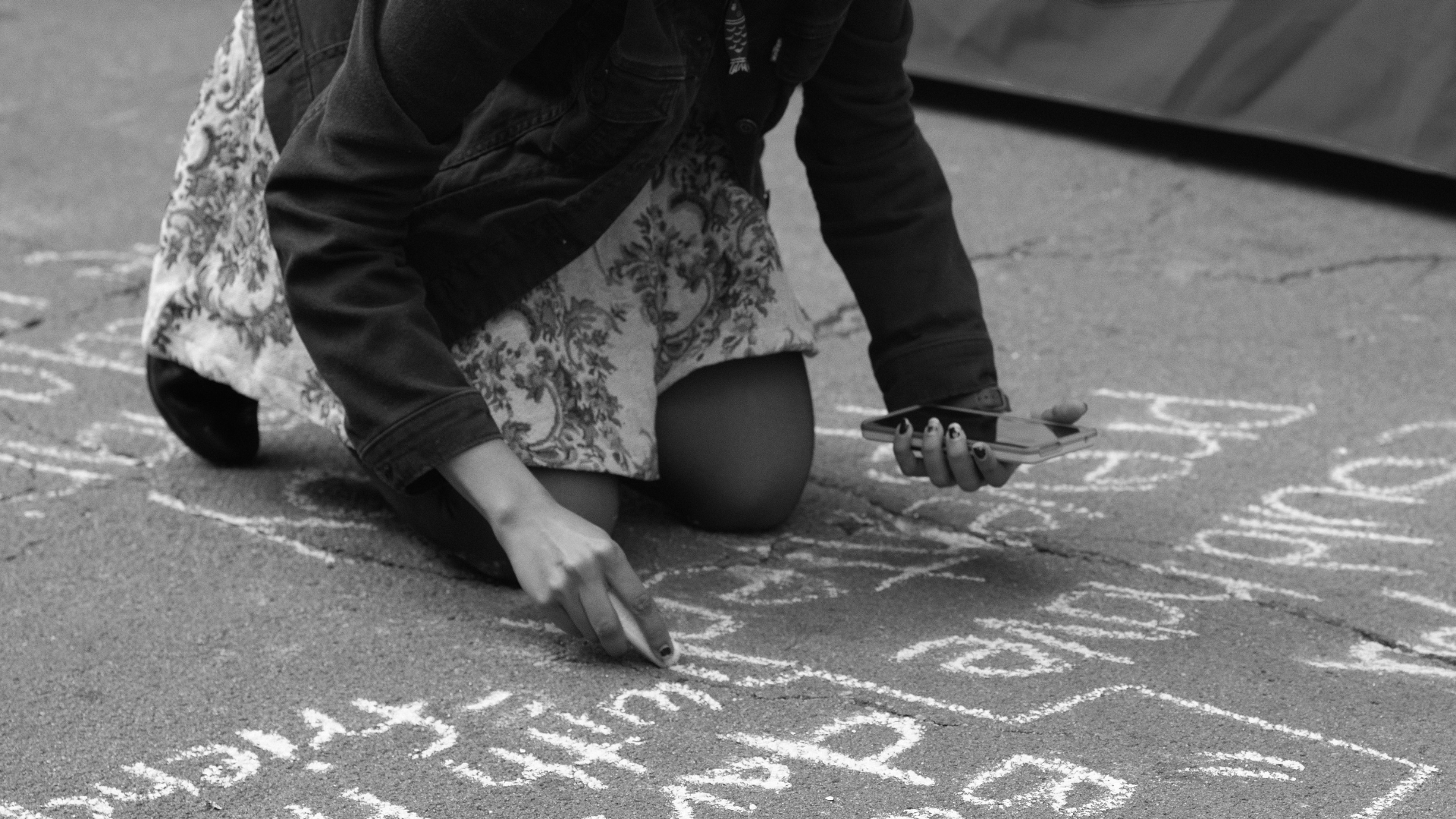 Young girl kneeling down writing a quote on the sidewalk using chalk.
