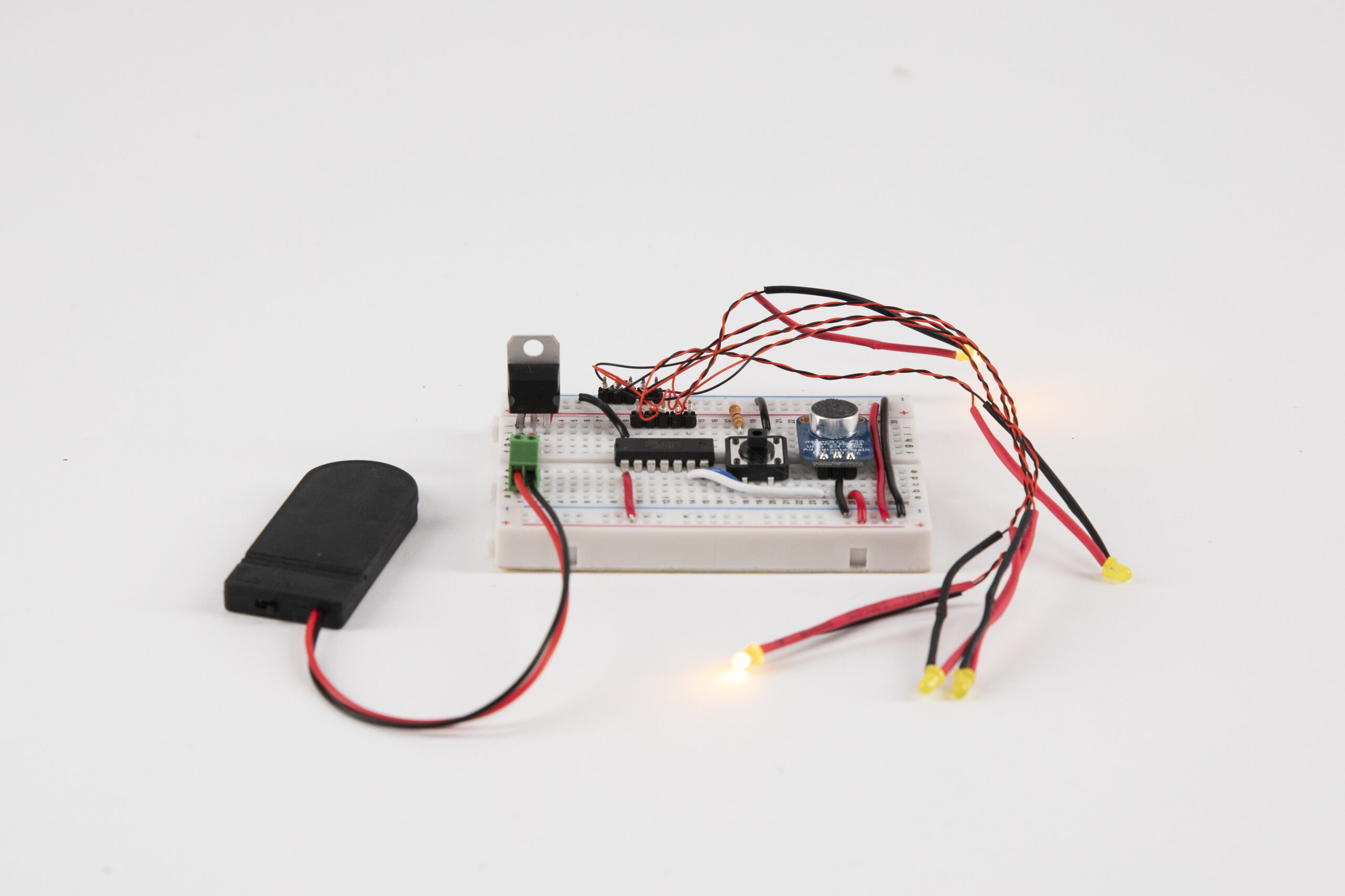 Breadboard with wires, voltage regulator, five yellow LEDs, microphone and battery pack connected to it.
