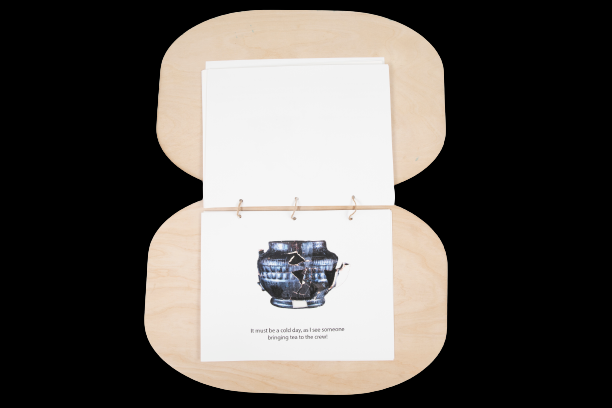 A book flipped open to a page with a teapot shown, including a piece of plastic that feels like a teapot. Text reads, 