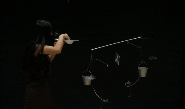 a person is placing a token into a bucket that is part of a dynamically moving kinetic mobile