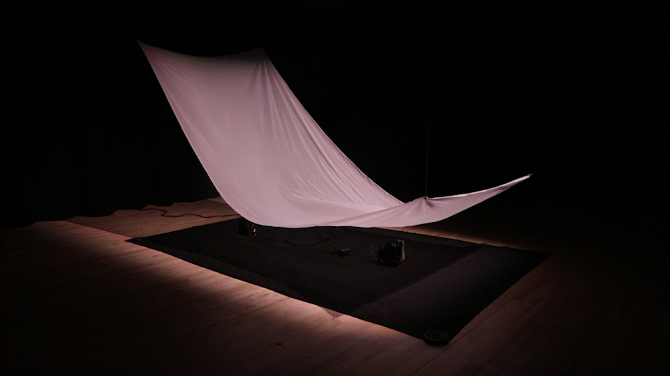 An animated gif of white chiffon fabric billowing because of the wind the two fans underneath are creating.