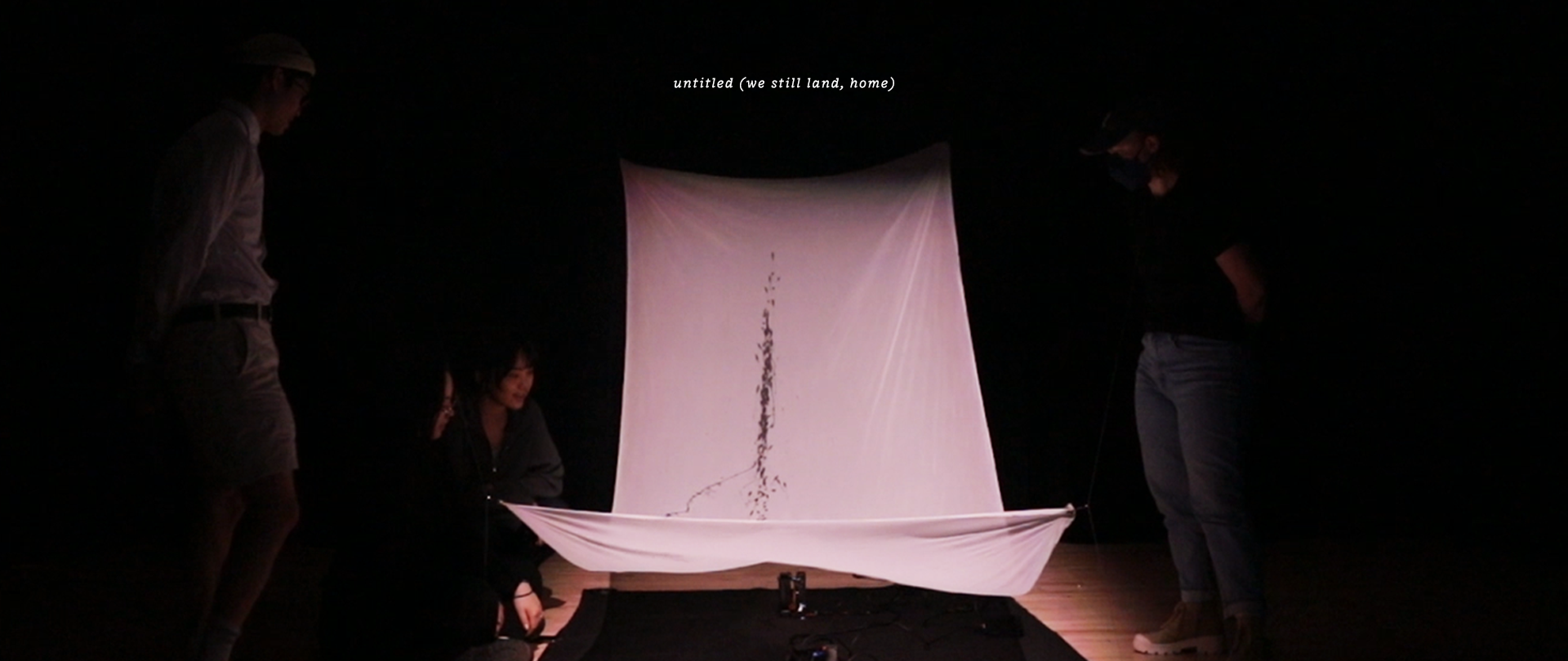 An image of four people watching and discussing the piece as trails of Chinese calligraphy ink make their way across the billowing fabric.