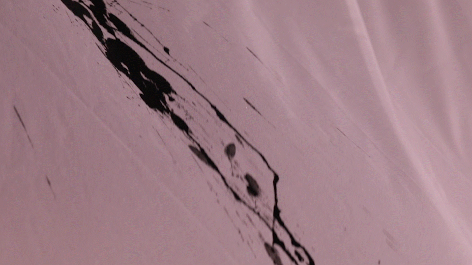 An animated gif of a close-up shot of ink dripping onto the fabric, scattering and leaving trails.