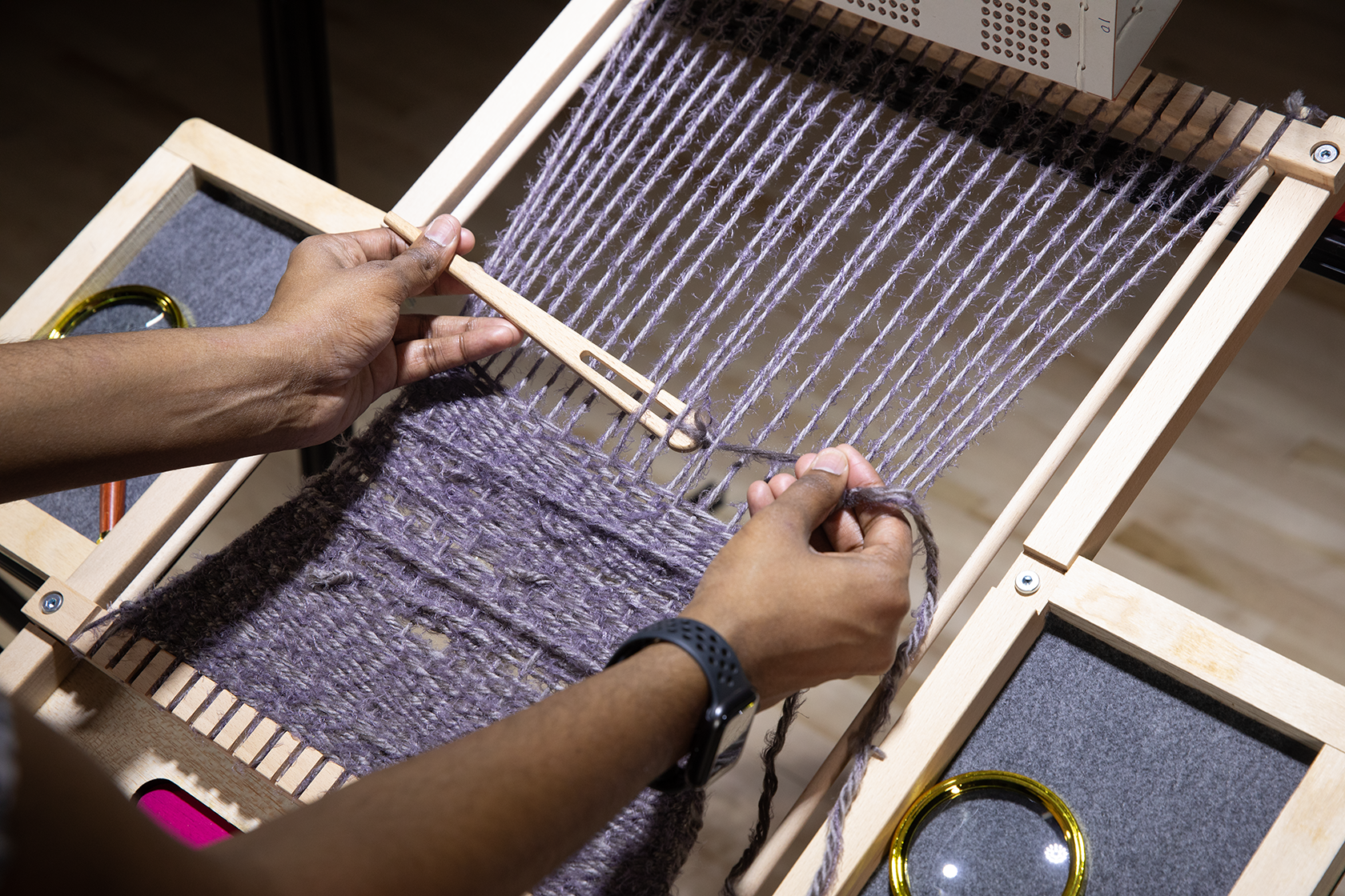 Close-up of the loom with the participant's hands weaving holding the shuttle while weaving
